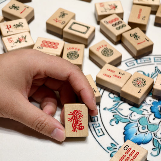 Hand holding a Wood Harmony flower tile above scattered wooden Mahjong tiles
