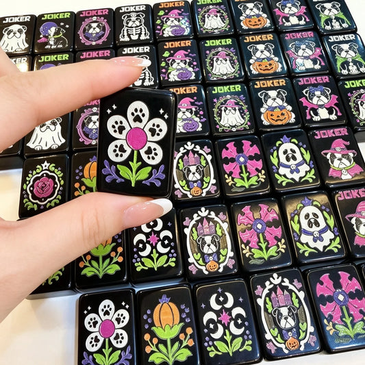 Hand holding a black Mahjong flower tile above Halloween bulldog jokers and illustrated tiles